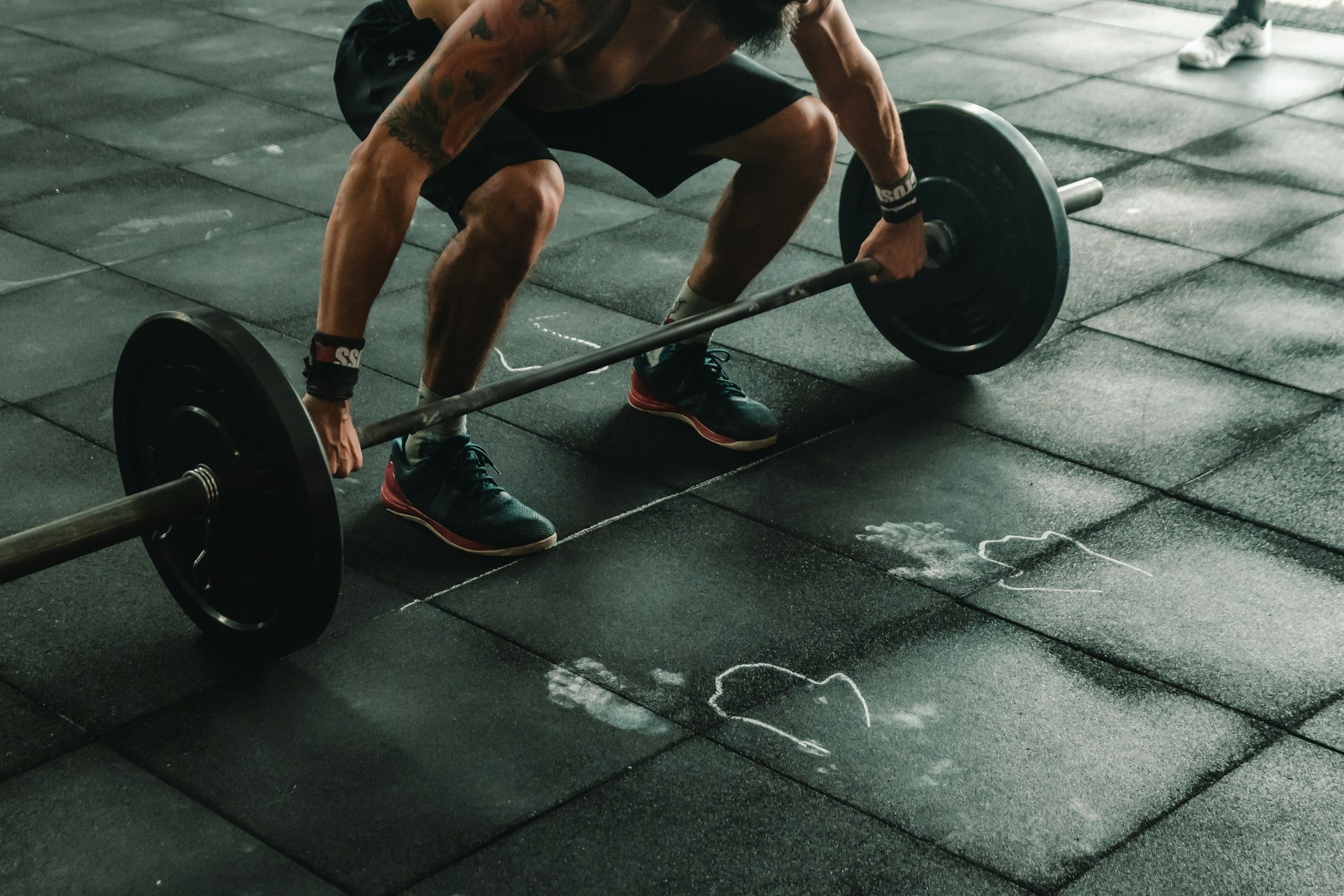 A man squats down to lift up a bar bell with weights in a dead lift